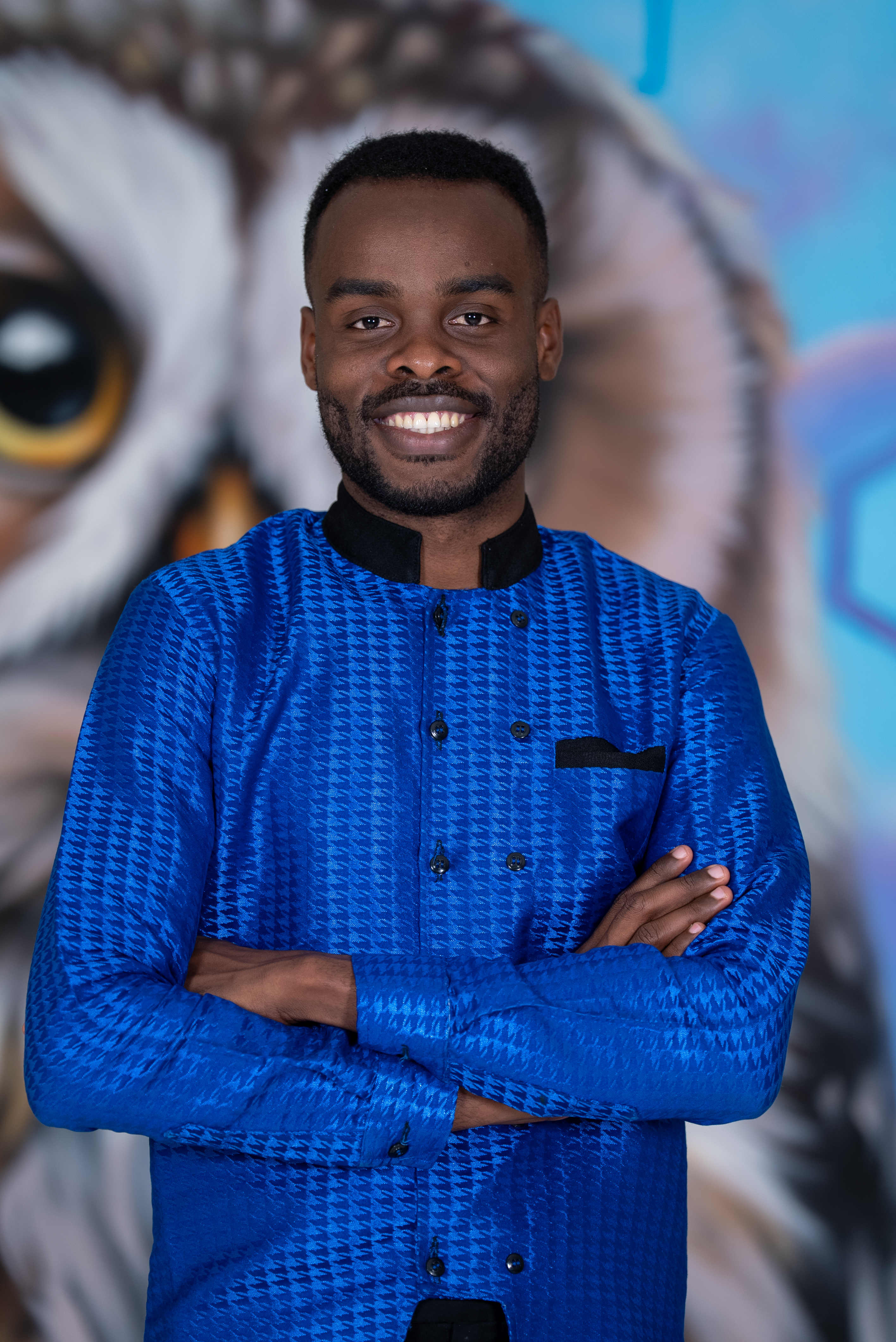 Samuel Kobina Gyasi in traditional attire, arms crossed, against a mural backdrop